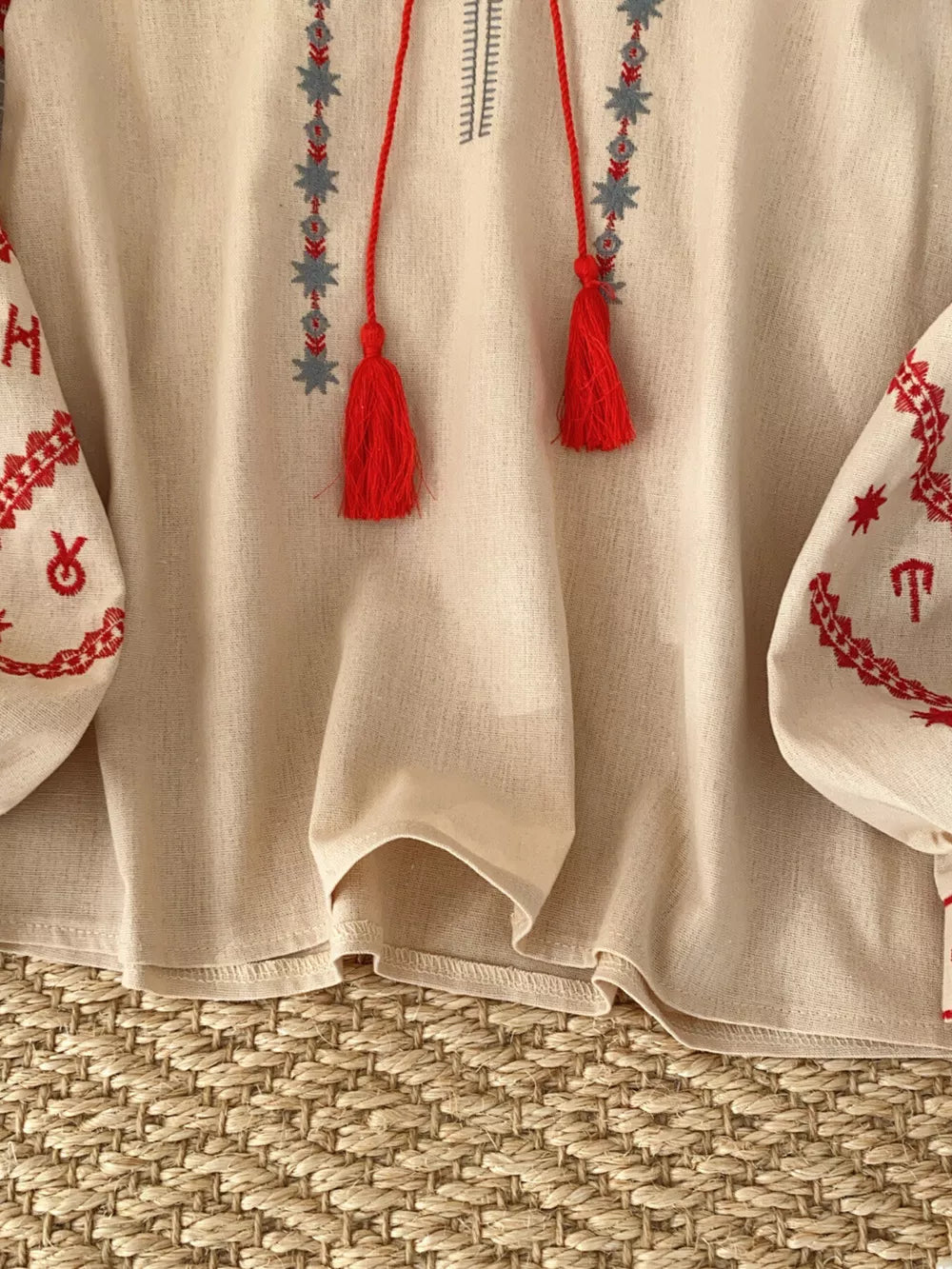 Apricot folk-inspired tie neck shirt with red embroidery and tassels.