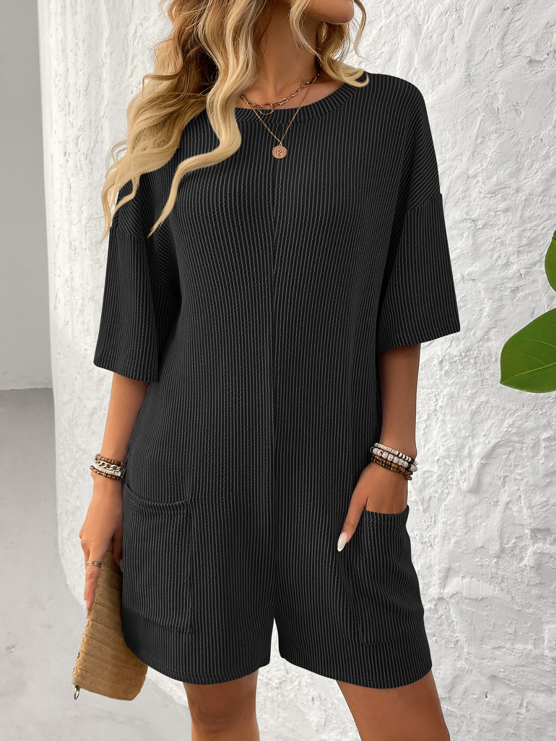 Black ribbed knit romper with short sleeves, crew neck, and front pockets.