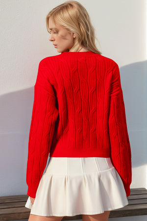 Red cable knit sweater with long sleeves and a crew neck, featuring a bow detail.