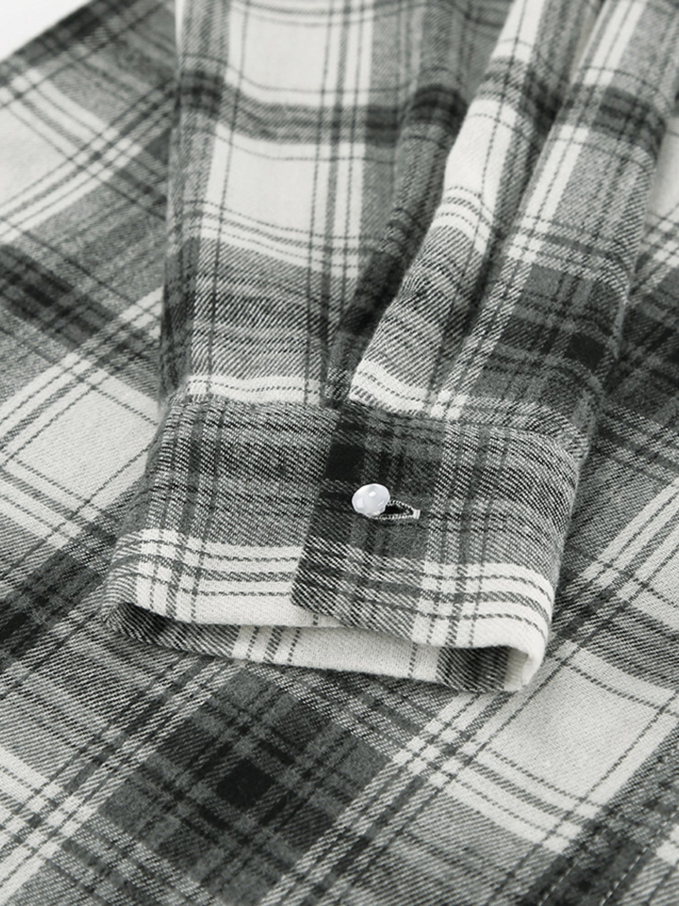 Button-up long sleeve cotton shirt in black and white plaid with a single button cuff detail.