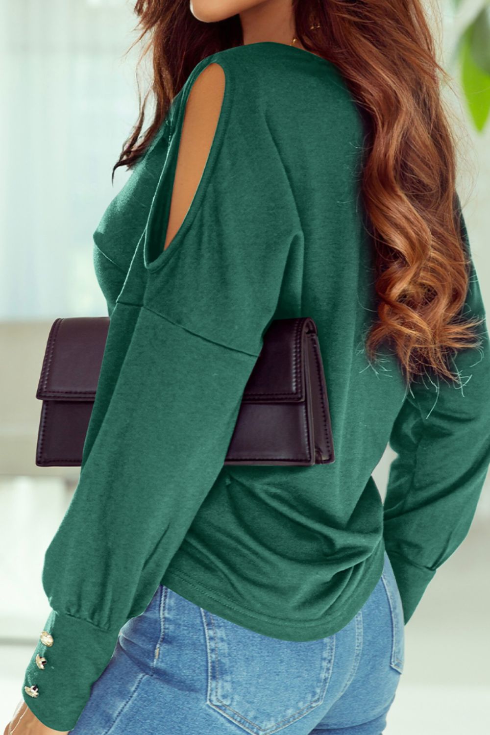Dark green shoulder-slit top with button cuffs and long sleeves, styled with jeans.