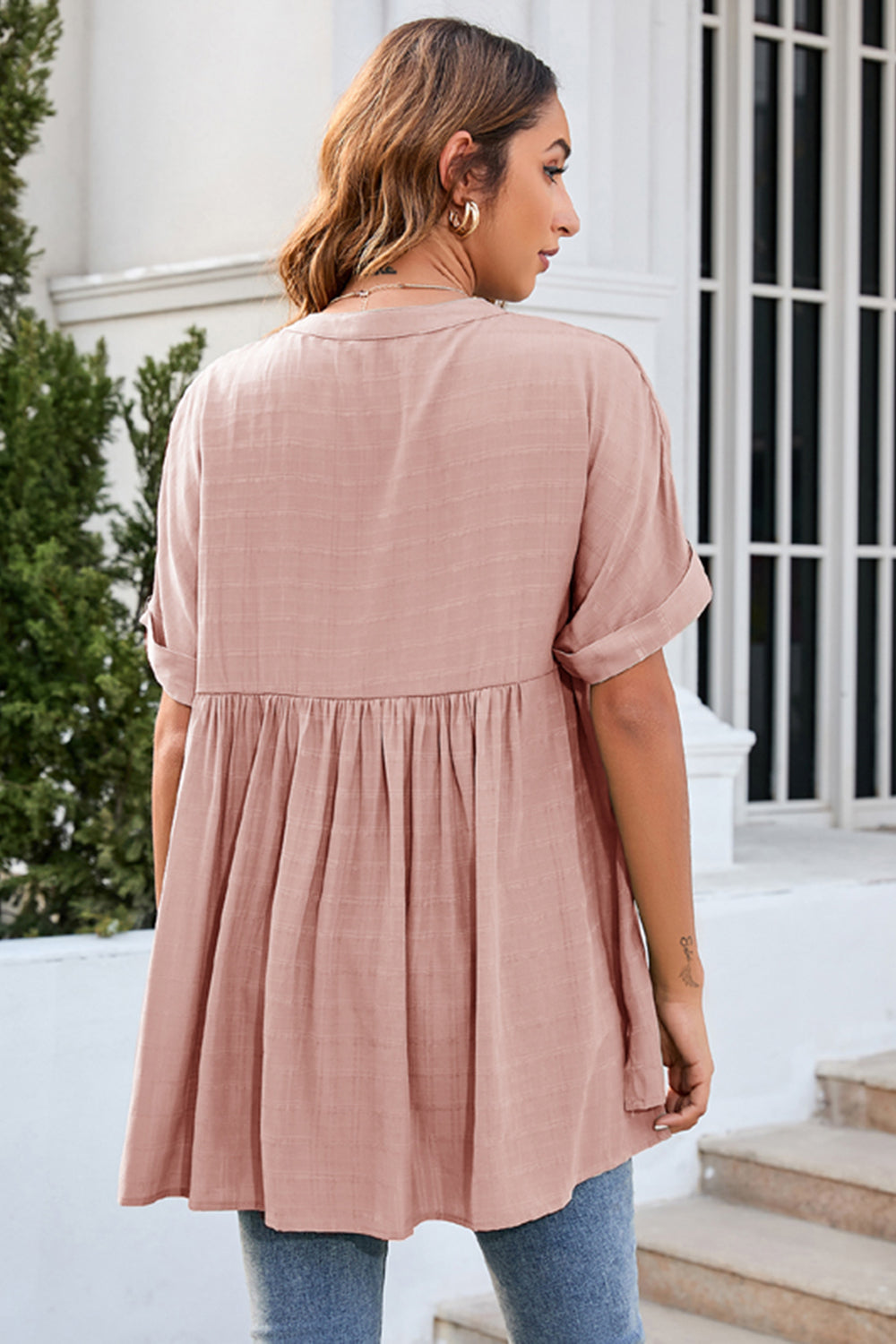 Blush pink blouse with gathered back yoke, rolled sleeves, and a flowy babydoll hem.