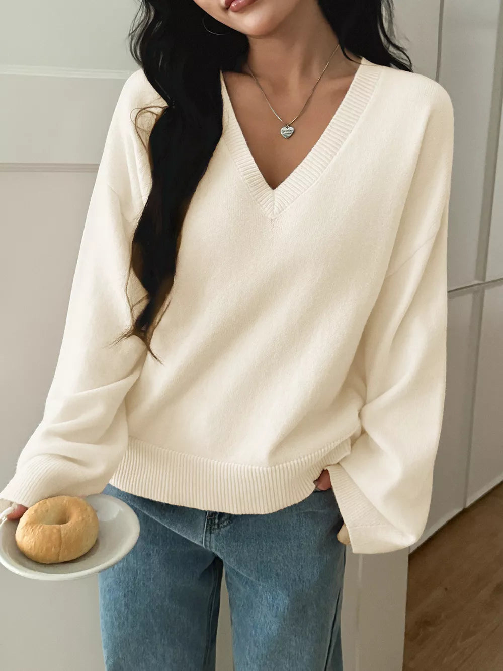 White V-neck knit sweater with ribbed cuffs and hem, styled with jeans.
