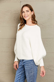 White ribbed dolman knit sweater with boat neck and balloon sleeves, styled with jeans.