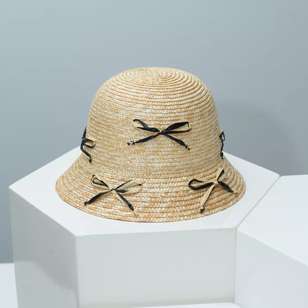Woven bucket hat in natural straw with black bowknot details.