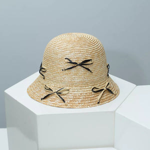 Woven bucket hat in natural straw with black bowknot details.