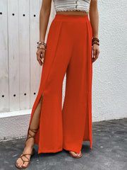 Orange-red textured palazzo trousers with dramatic thigh-high slits and a wide leg.