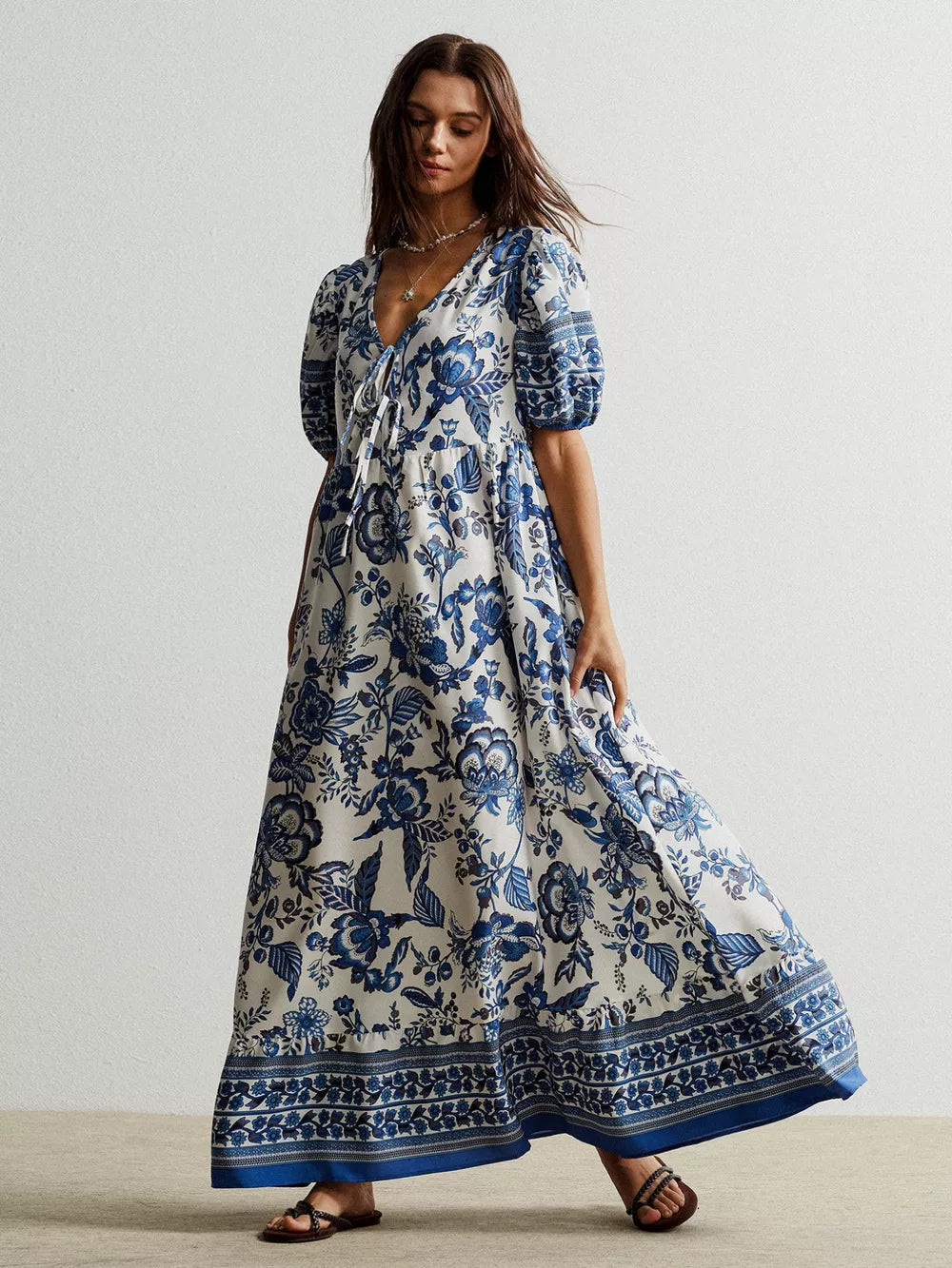 Maxi dress with blue floral print, tie-neck, puff sleeves, and tiered skirt.