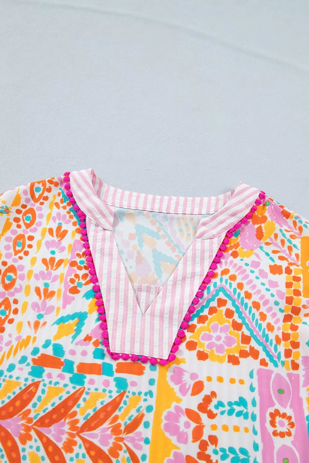 Vibrant patchwork print blouse with pink striped V-neck and pompom trim