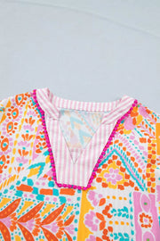 Vibrant patchwork print blouse with pink striped V-neck and pompom trim