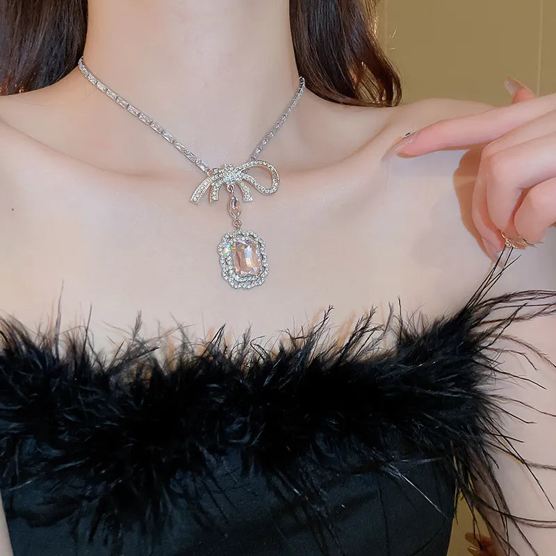 Silver bow pendant necklace with crystal accents and a rectangular pink gem.