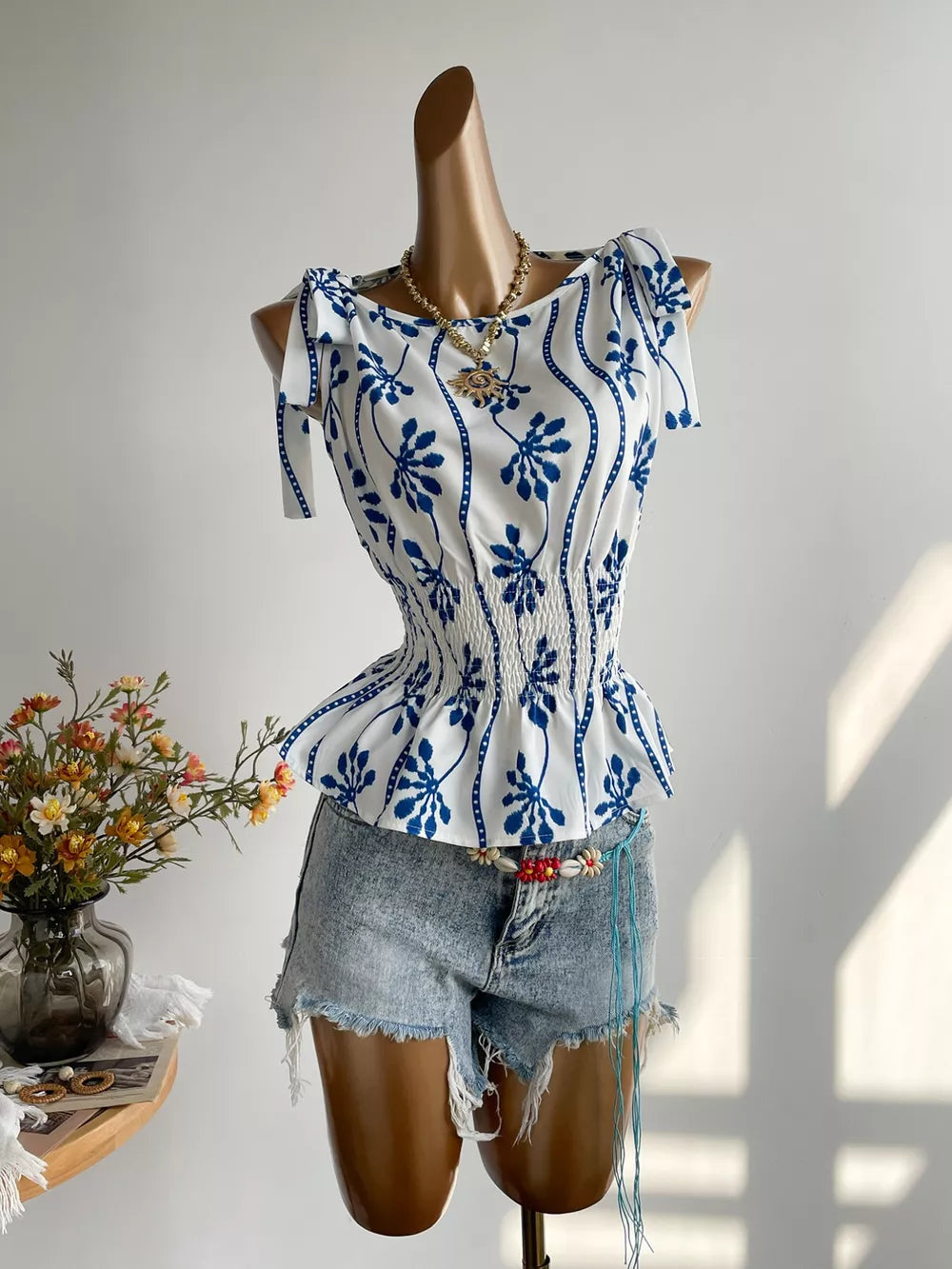 White and blue botanical print smocked blouse with tie shoulder straps and boat neckline.