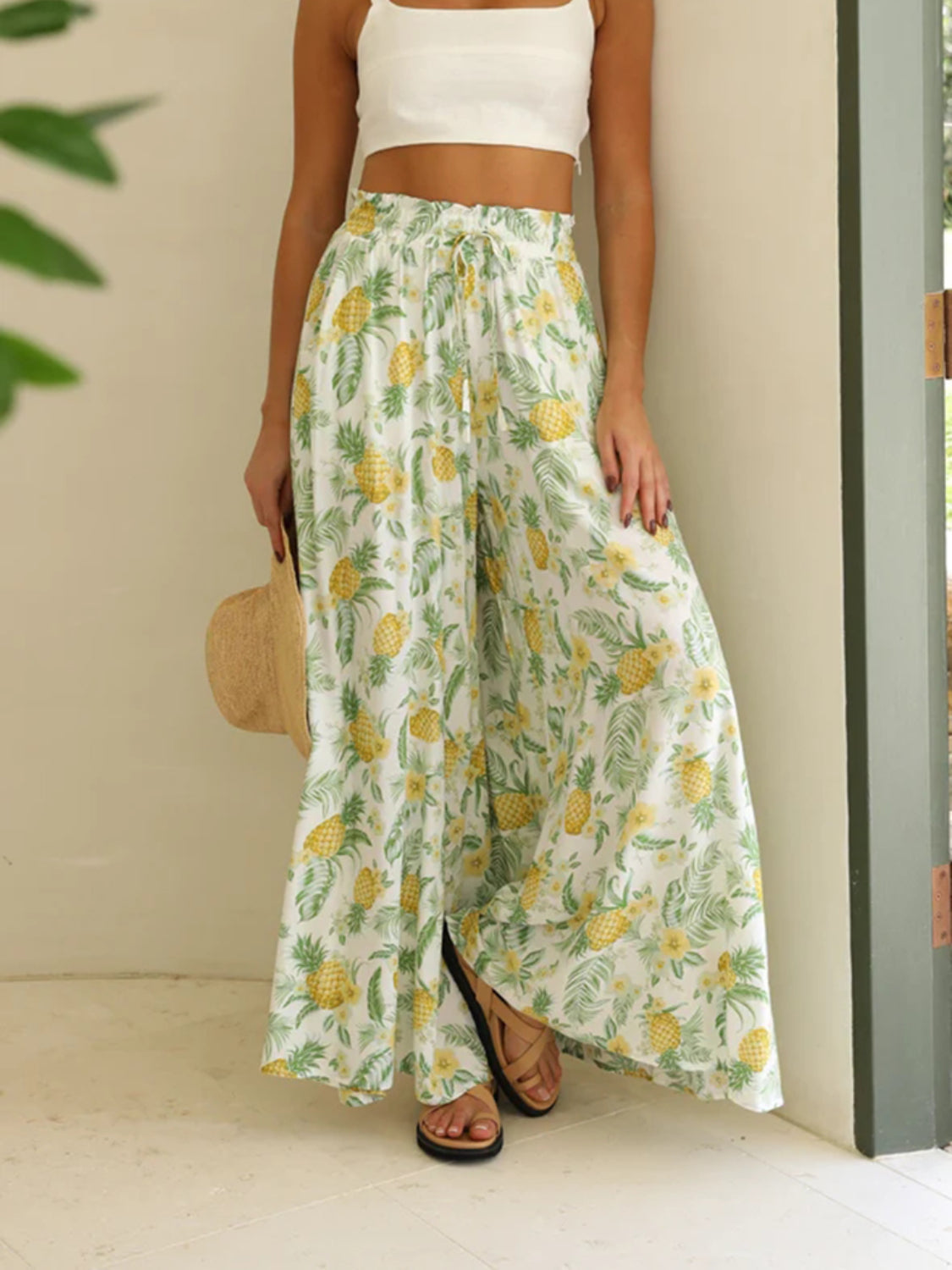 White palazzo trousers with a yellow pineapple and green leaf print, featuring a drawstring waist and side slits.