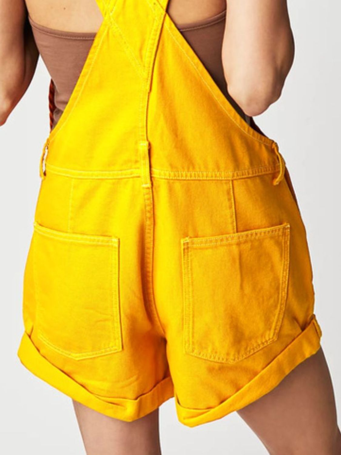 Gold denim short overalls with cuffed hems and crisscross straps.