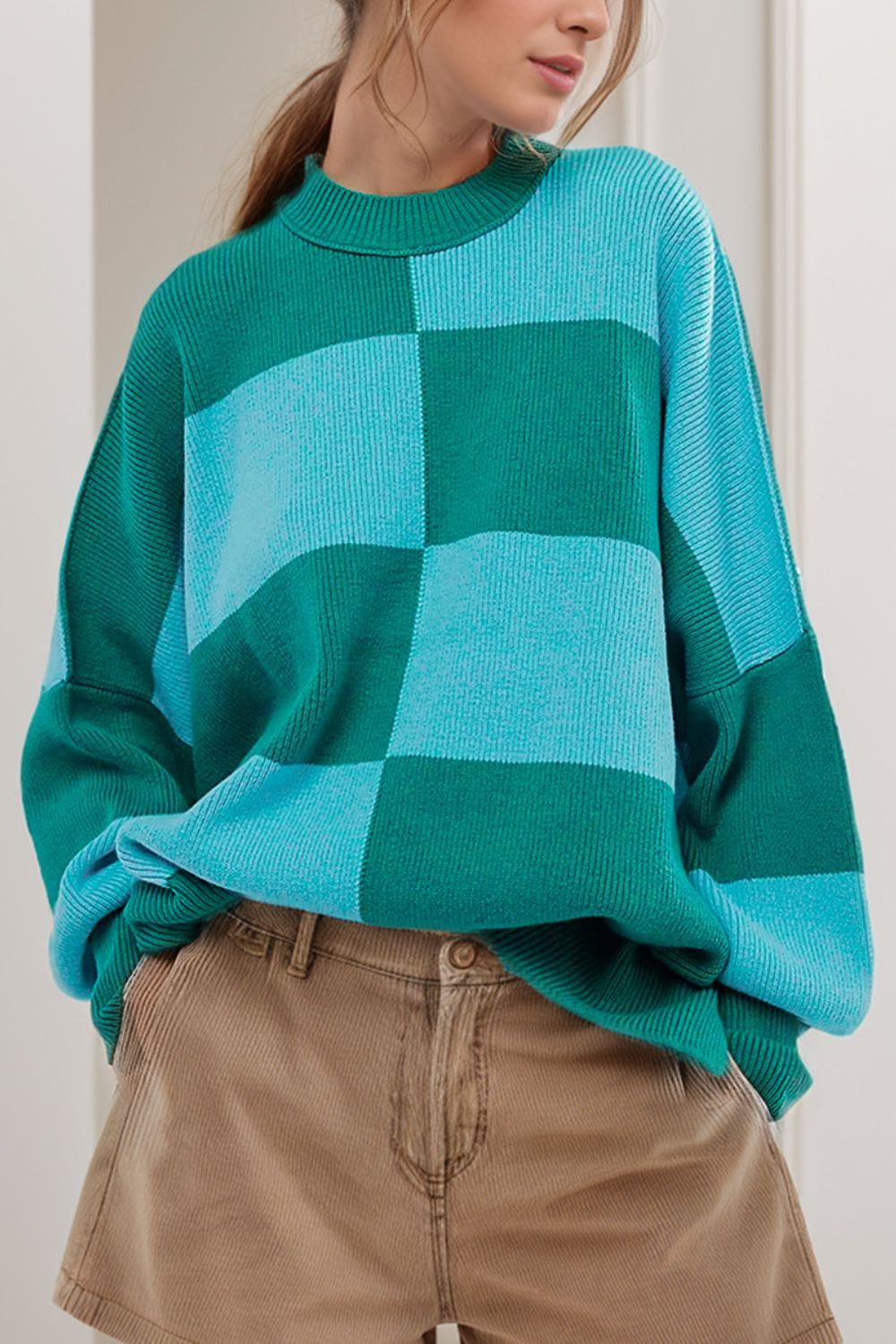 Checkerboard knit oversized sweater in turquoise and green with a mock neck and long sleeves.
