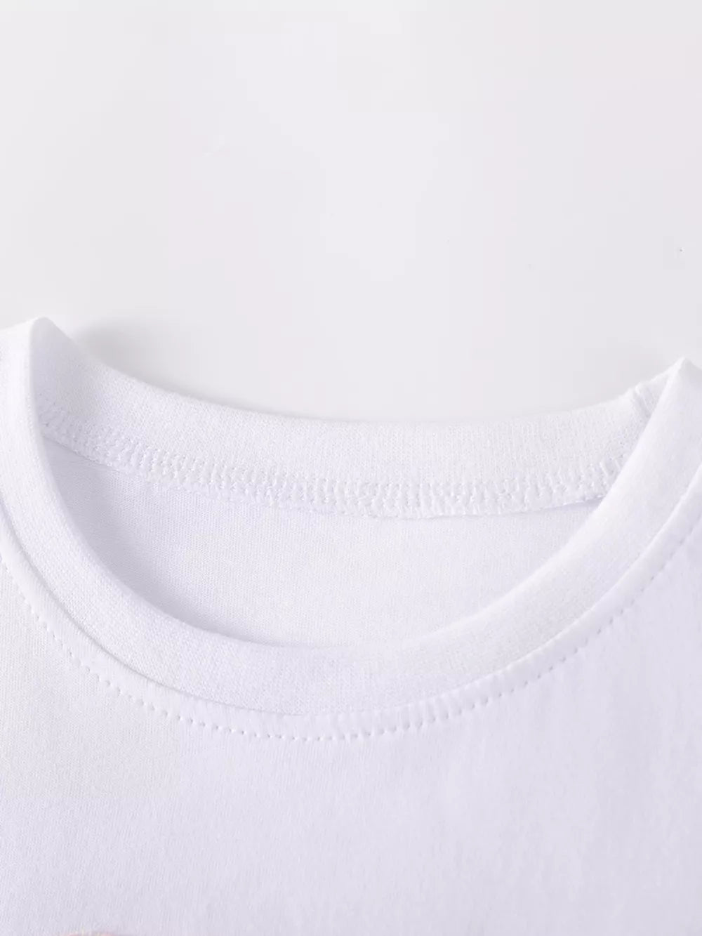 White baby dress neckline detail, cotton fabric with rainbow heart applique.