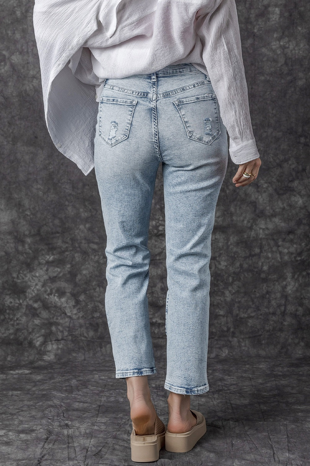 Light wash distressed denim jeans with a slim leg cut, shown from the back.