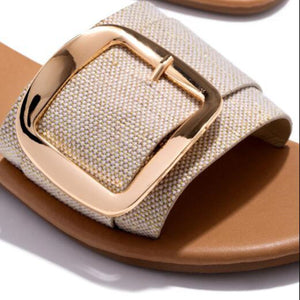 Beige slide sandals with gold buckle detail and textured strap.