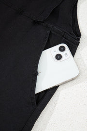 Black denim romper with adjustable straps and a pocket holding a smartphone.