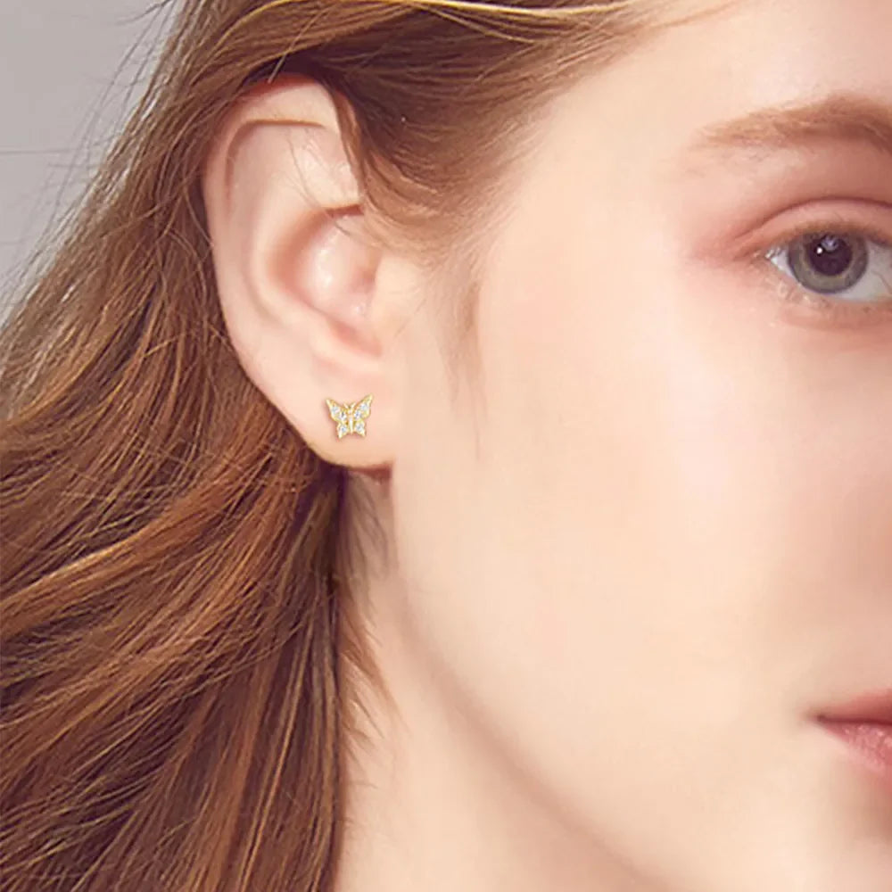 Gold moissanite butterfly stud earrings with clear stones, shown on ear.