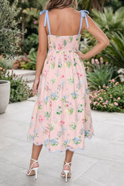Pink midi dress with wildflower print, smocked bodice, and blue tie straps.