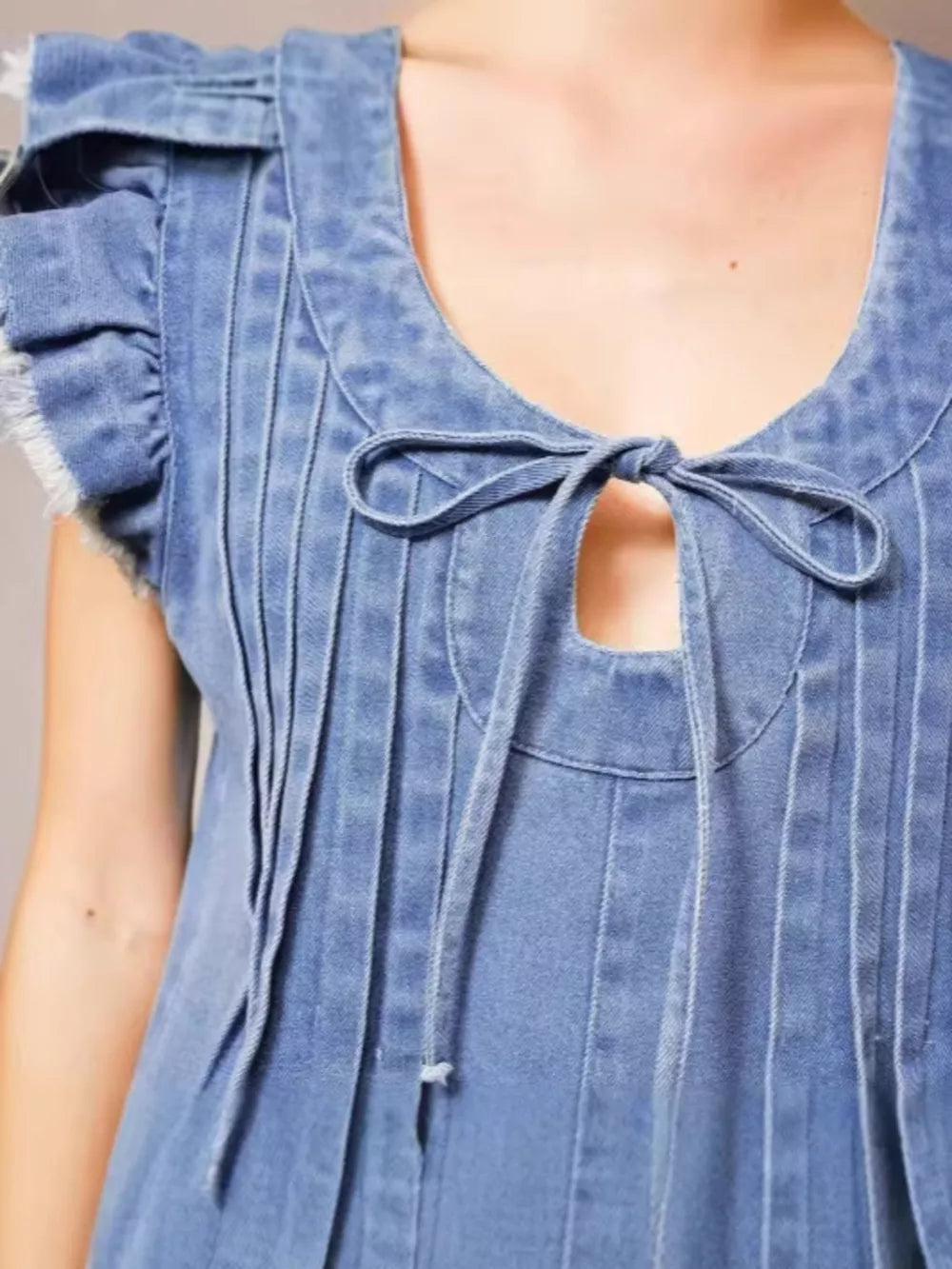 Denim romper with tie neck, ruffled sleeves, and frayed edges.