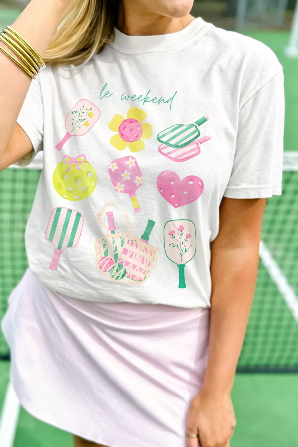 White polyester t-shirt with playful pickleball and floral graphic print and "le weekend" text.