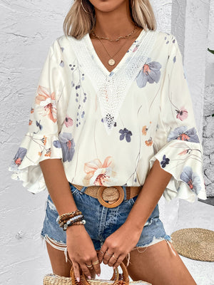 White floral bell sleeve blouse with lace V-neck detail and ruffled cuffs.