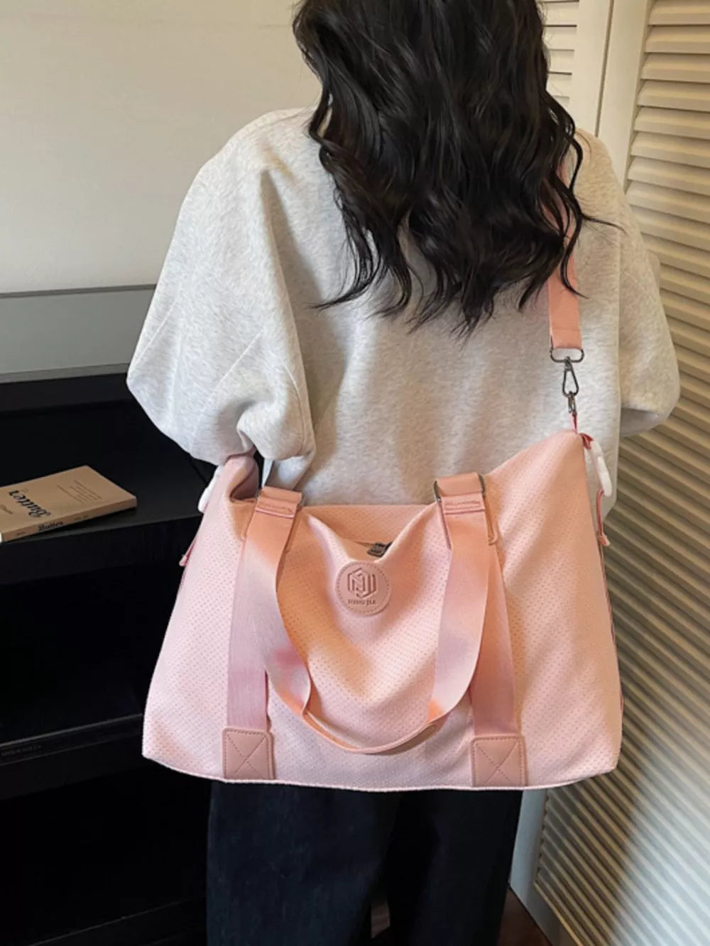 Chic perforated large duffle bag in pink with dual handles and a crossbody strap.