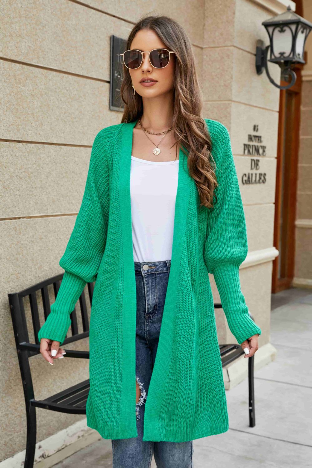 Green knit cardigan with puffed sleeves and open front, styled with jeans.