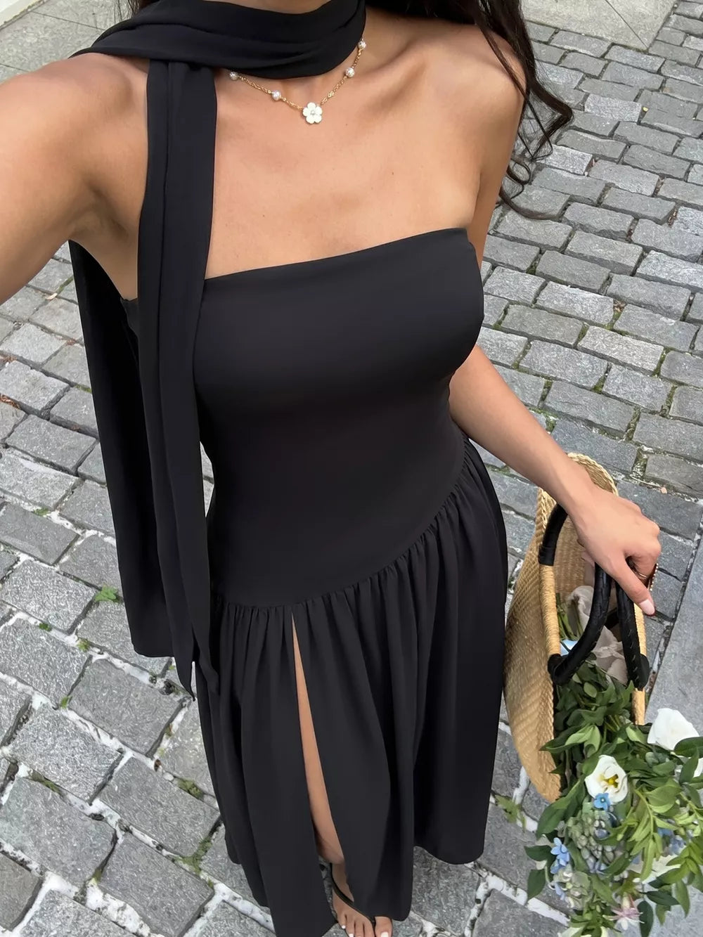 Black strapless maxi dress with asymmetrical hem, high slit, and matching scarf detail.
