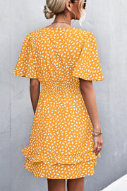 Mustard mini dress with white speckle print, flutter sleeves, smocked waist, and ruffled hem.
