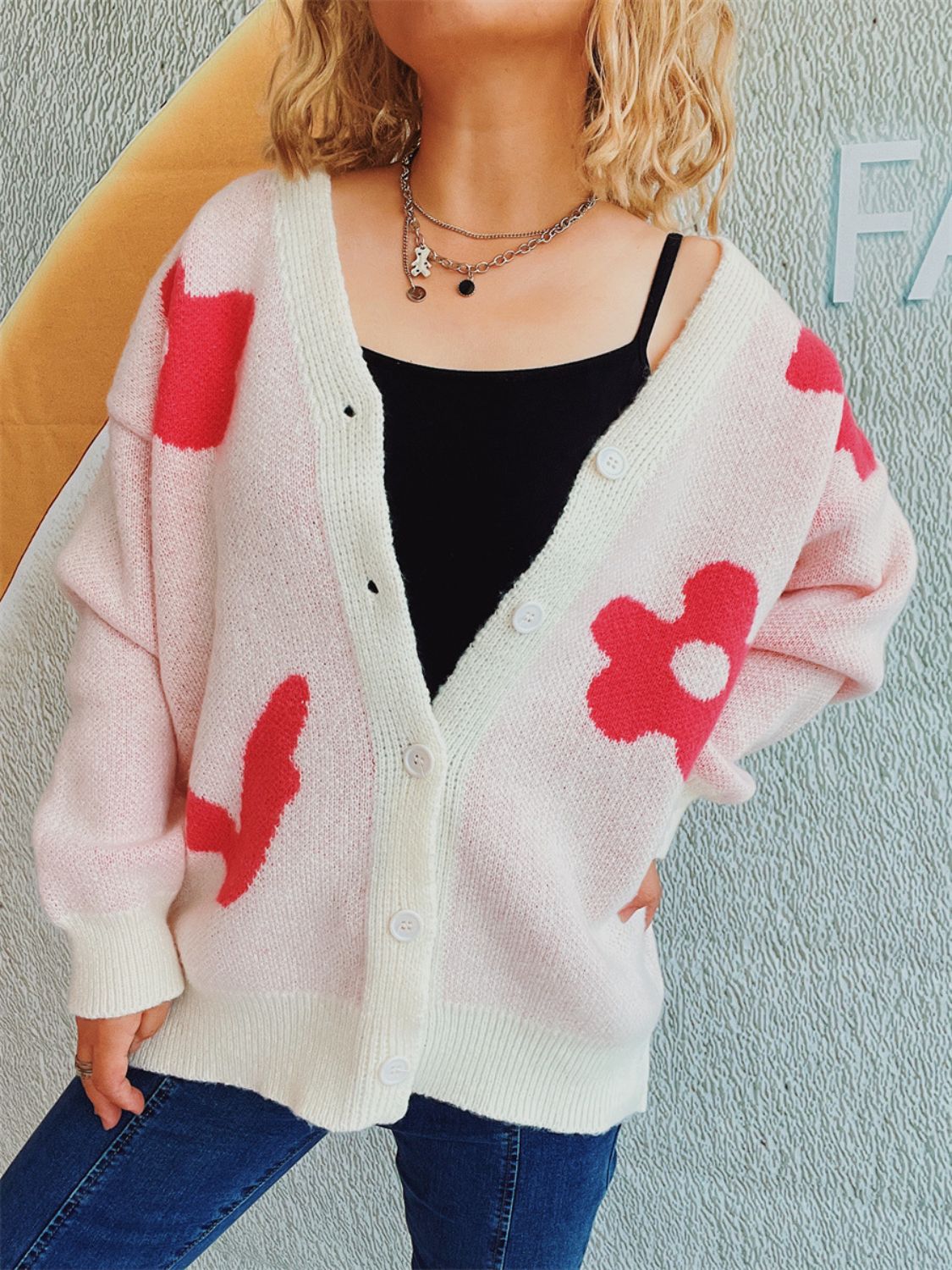 Blush pink acrylic cardigan with playful red floral appliqué and white trim.