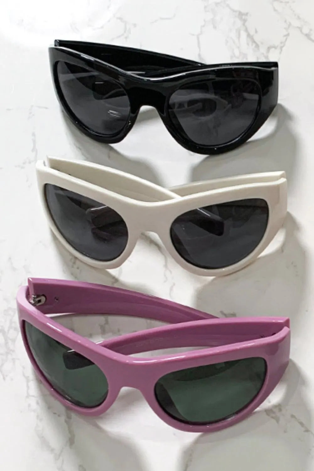 Sporty shield sunglasses in black, beige, and dusty pink with dark lenses.
