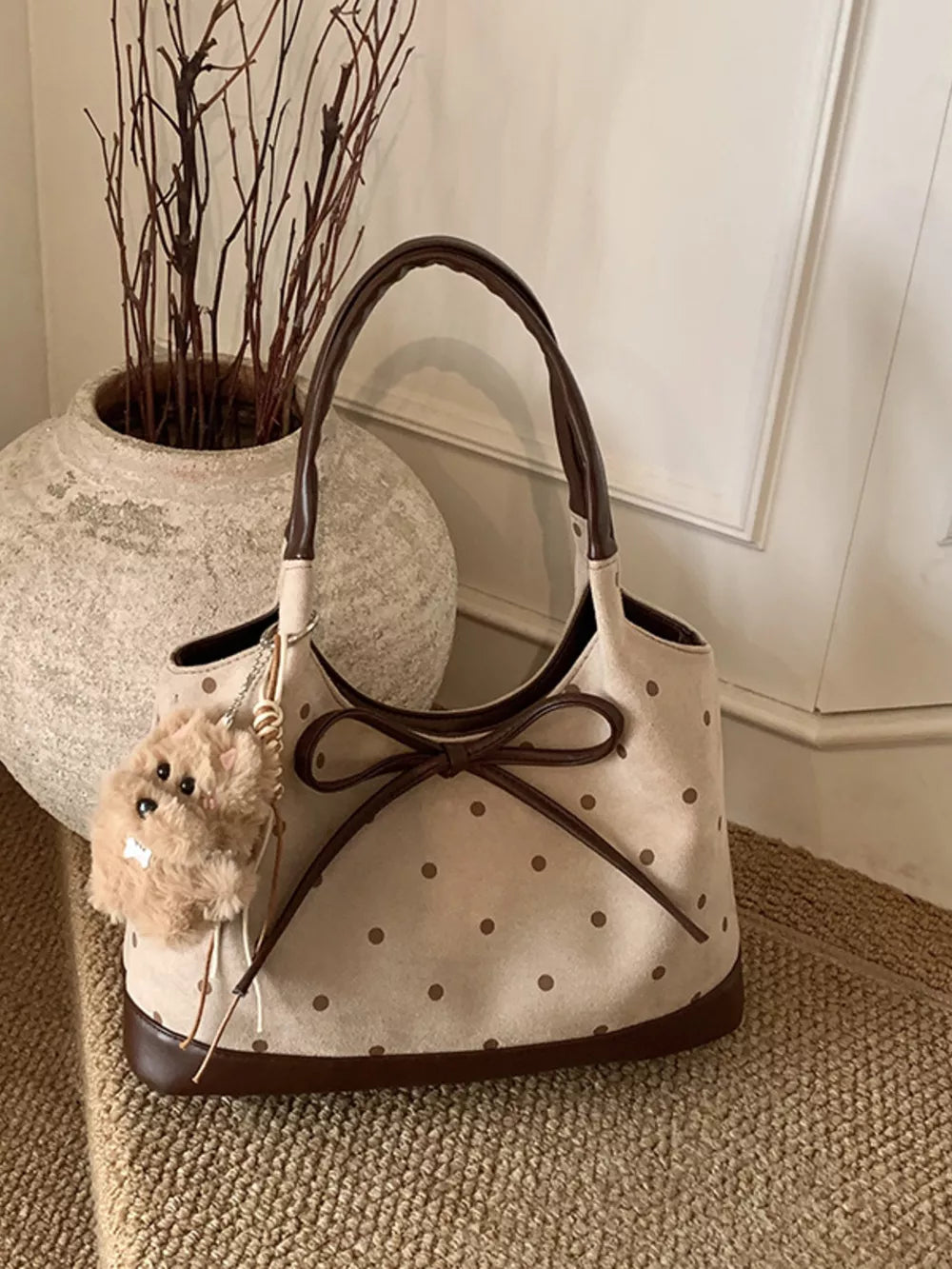 Tan polka dot shoulder bag with brown trim, bow detail, and fuzzy charm.