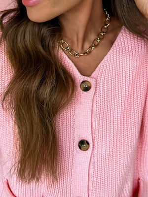 Pink acrylic button front V neck sweater vest with brown buttons.