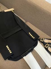 Black double-breasted tailored blazer with gold buttons, styled with white pants and embellished heels.