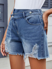 Medium wash denim shorts with asymmetric wrap, shredding and frayed hem.