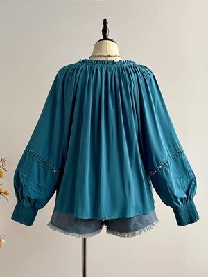 Teal ruffled lantern sleeve blouse with cutout detail and smocked cuffs, styled with denim shorts.