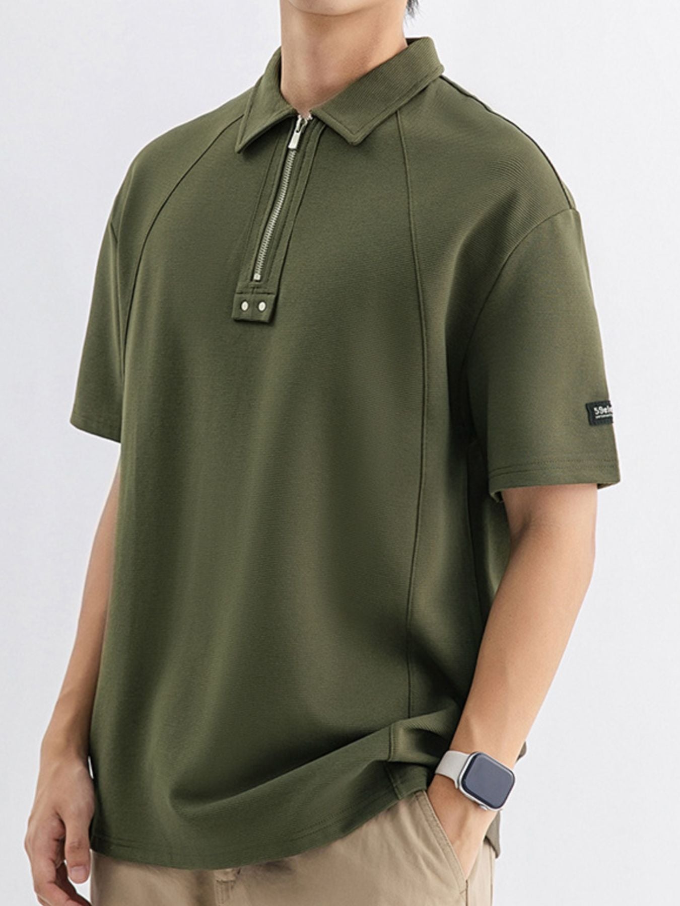 Army green cotton polo with metallic half-zip and button details.