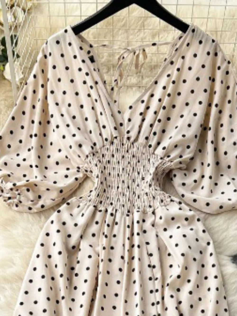 Beige polka dot smocked romper with V-neck and tie back.