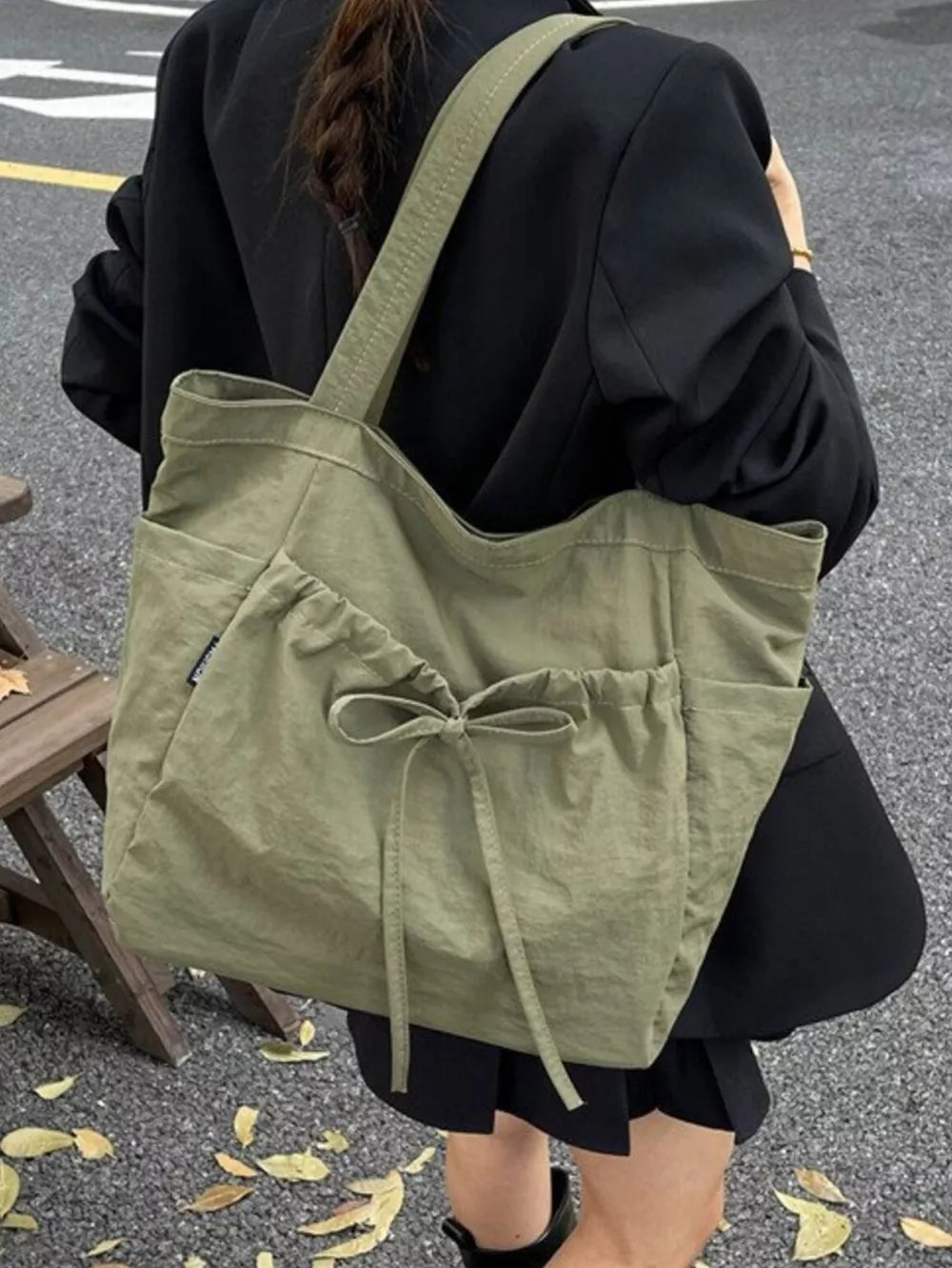 Olive green nylon tote bag with drawstring and bow detail, featuring exterior pockets.