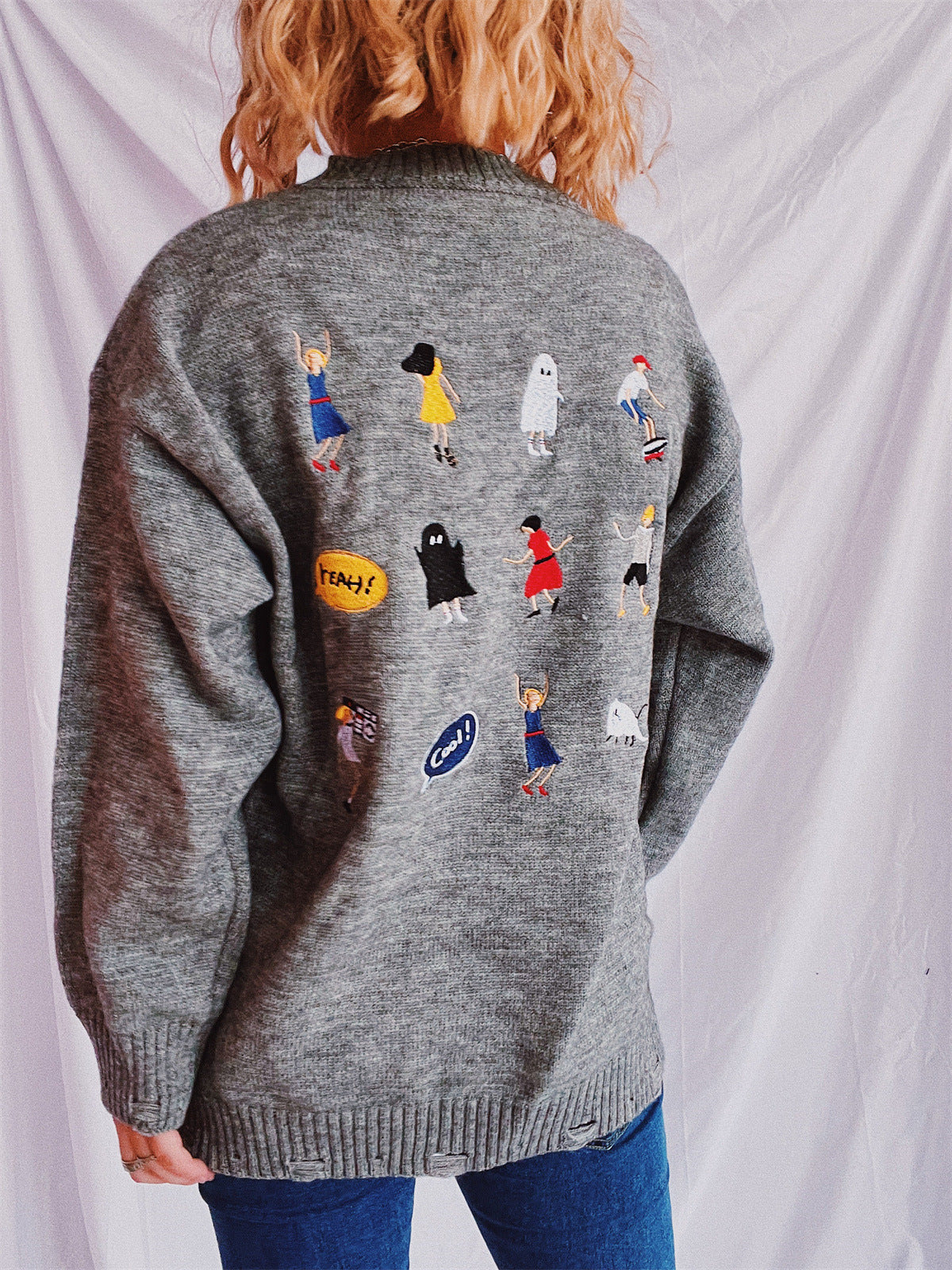 Dark gray relaxed knit sweater with embroidered characters and patches.