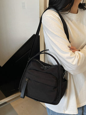 Black crossbody bag with decorative pull tab and multiple zippered pockets.