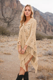 Tan knit poncho with geometric pattern, fringe, and tie neck, styled with jewelry.