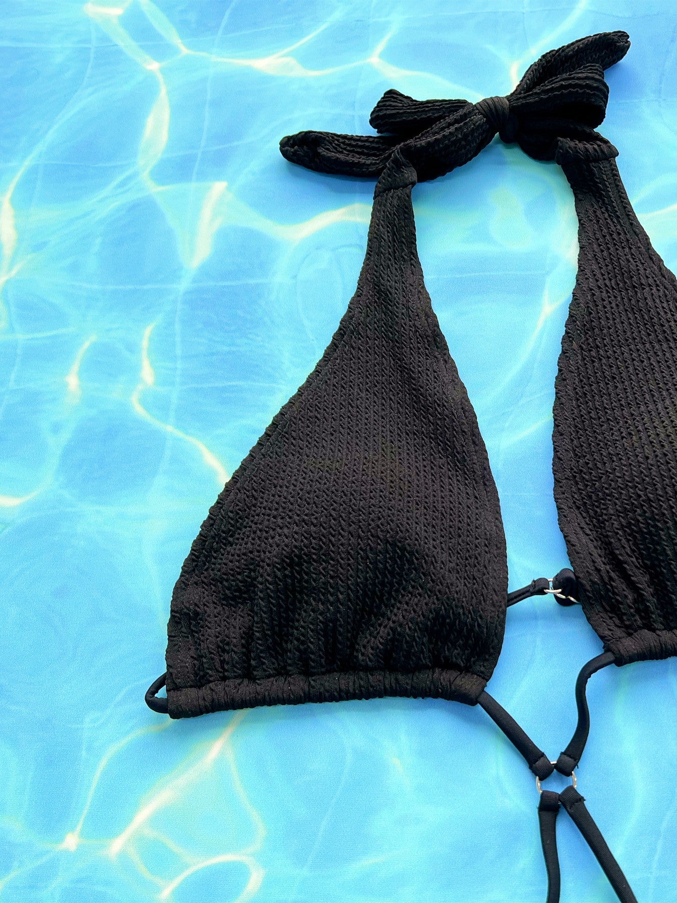 Black textured halterneck swimsuit with cutout detail and tie closure.