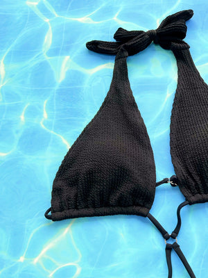 Black textured halterneck swimsuit with cutout detail and tie closure.