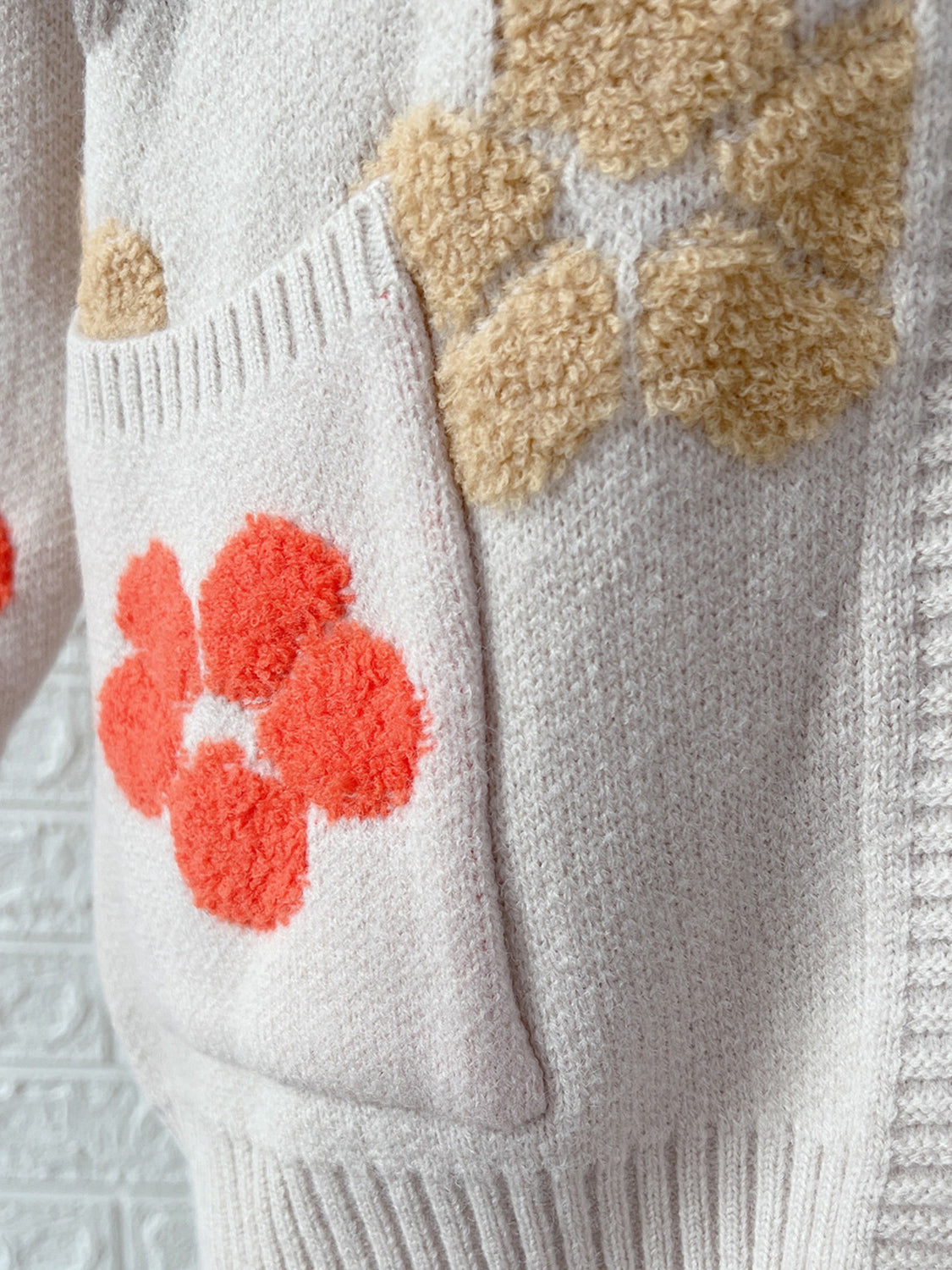 White knit cardigan with textured floral appliqués in coral and tan.