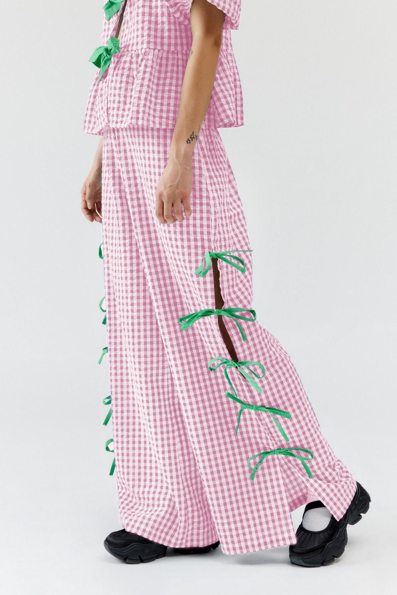 Blush pink gingham wide-leg trousers with green bow details down the side seams.