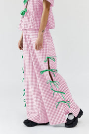 Blush pink gingham wide-leg trousers with green bow details down the side seams.